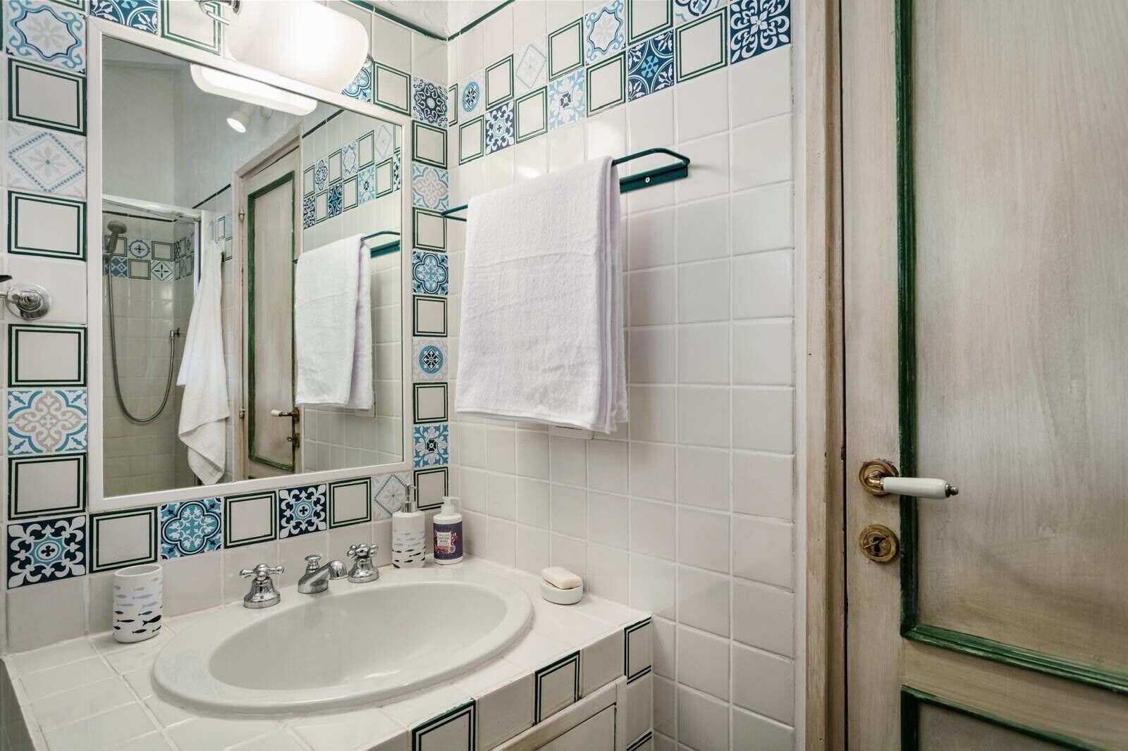 Een badkamer met een witte wastafel, een spiegel, een handdoekhouder en een douche.