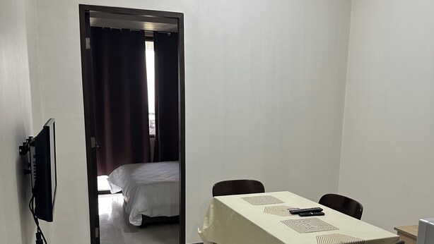 Ein Hotelzimmer mit Esstisch, Stühlen, Fernseher und einem Bett im Hintergrund.