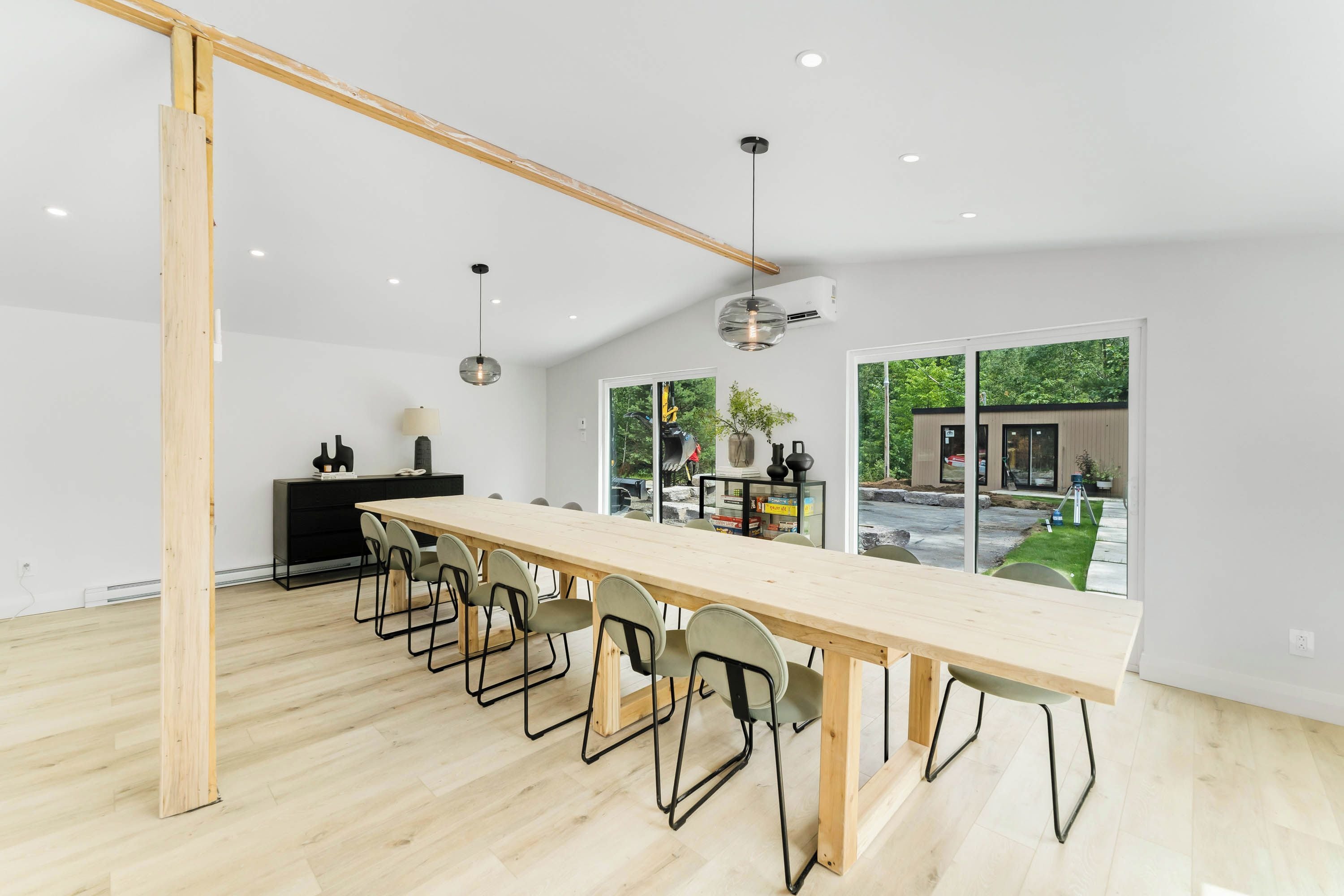 A modern conference room with a long wooden table, black chairs, and a glass wall offering a view of the outdoors.