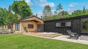 Una moderna baita con facciata in legno, un patio con vasca idromassaggio e un'ampia finestra.