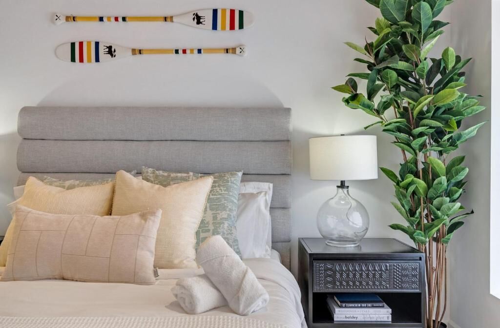 A neatly made bed with pillows, a bedside table with a lamp, and a plant.