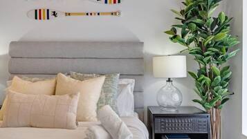 A neatly made bed with pillows, a bedside table with a lamp, and a plant.