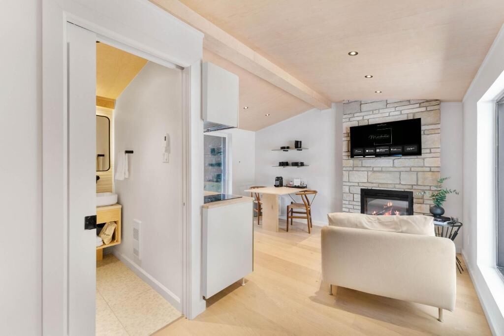 A modern living room with a fireplace, a television mounted on the wall, and a dining area with a table and chairs.
