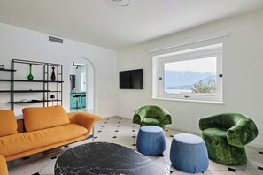 Ein modernes Wohnzimmer mit einer Couch, Hocker und einem Fernseher an der Wand.