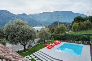 Ein Swimmingpool mit roten Liegestühlen, Blick auf Berge und einen See.