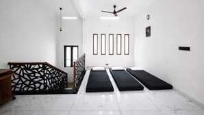 Ein modernes Zimmer mit drei schwarzen Betten, einem Holztisch, einem Deckenventilator und einem geometrischen Wandmuster.