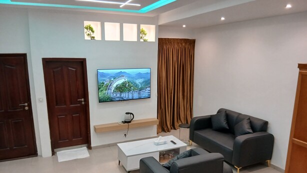 Una sala de estar moderna con una televisión de pantalla plana montada en la pared, un sofá de cuero negro, una mesa de centro y un taburete pequeño y redondo.