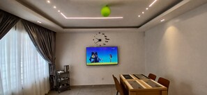 Ein modernes Wohnzimmer mit Flachbildfernseher, einem Esstisch und einer Deckenleuchte.