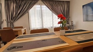 Un salón de conferencias con una gran mesa, sillas, un florero con flores rojas y una pantalla de televisión mostrando un evento.