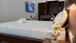 Habitación de hotel con cama, televisor montado en la pared, escritorio de madera y planta en maceta.