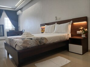 Ein modernes Hotelzimmer mit einem großen Bett, Nachttischen, einem Schreibtisch und einem Fenster mit Vorhängen.