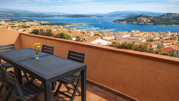 Une terrasse avec une table et des chaises, offrant une vue sur une ville côtière et la mer.