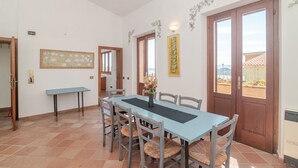 Un coin repas avec une table et des chaises, un vase rempli de fleurs et une vue sur l’extérieur, visible à travers la porte.