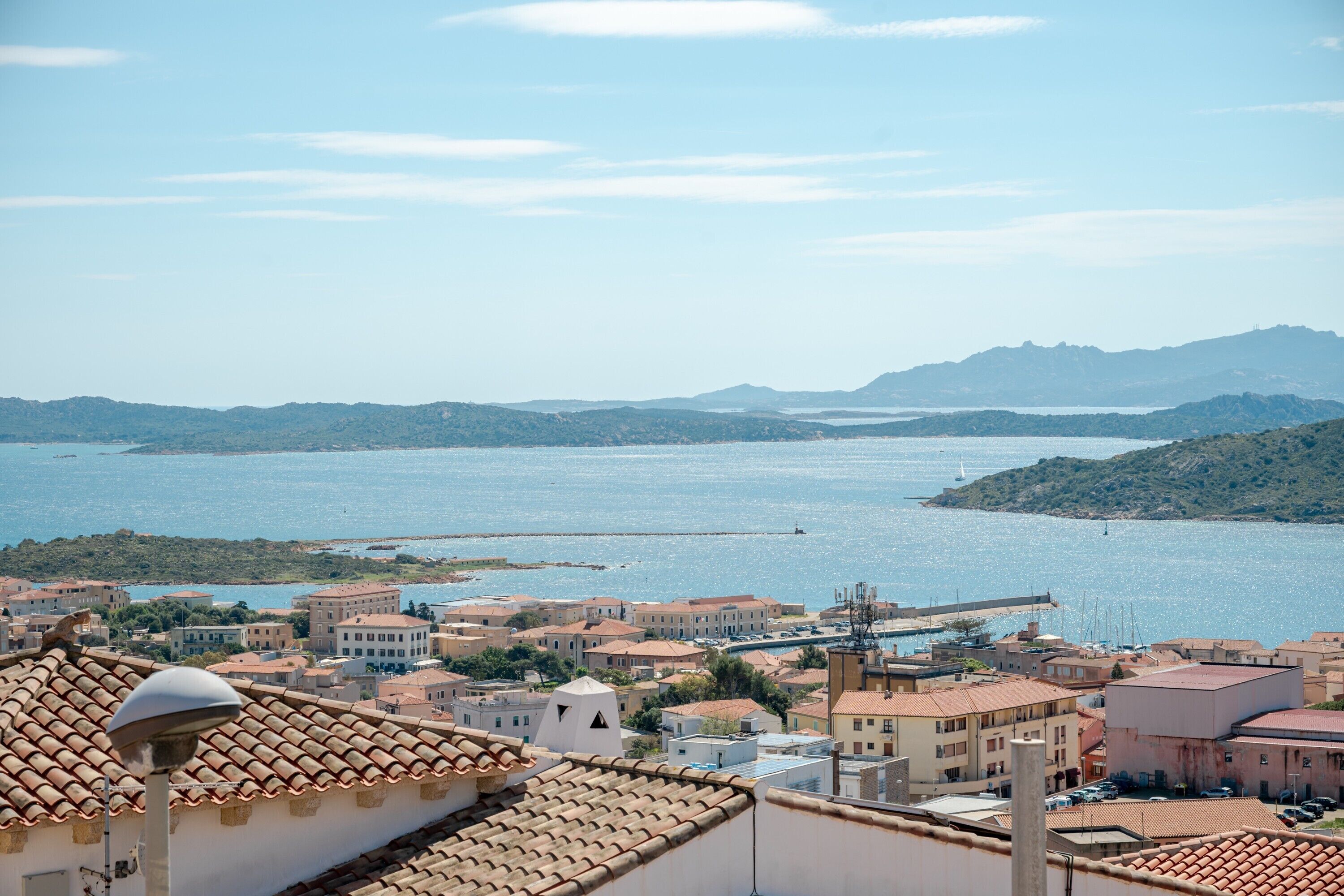 A coastal town with terracotta-roofed buildings, a marina, and a large body of water.