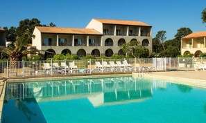 Ein Pool mit Liegestühlen und ein Gebäude mit Bogenfenstern im Hintergrund.