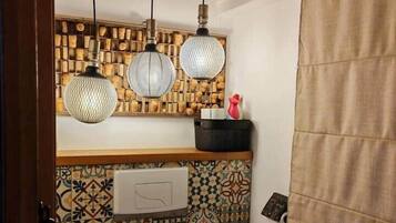 Une salle de bain avec un mur recouvert de carreaux décoratifs, des toilettes et trois lampes suspendues.