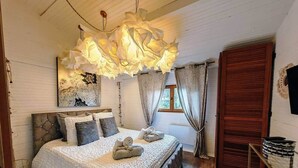Een slaapkamer met een groot bed, een hanglamp, een houten hoofdbord, een raam met gordijnen en een houten deur.