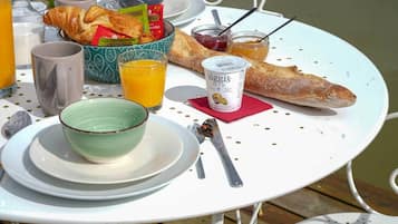 Una mesa de desayuno con cruasanes, un vaso de jugo de naranja, un tazón de yogur y una baguette.