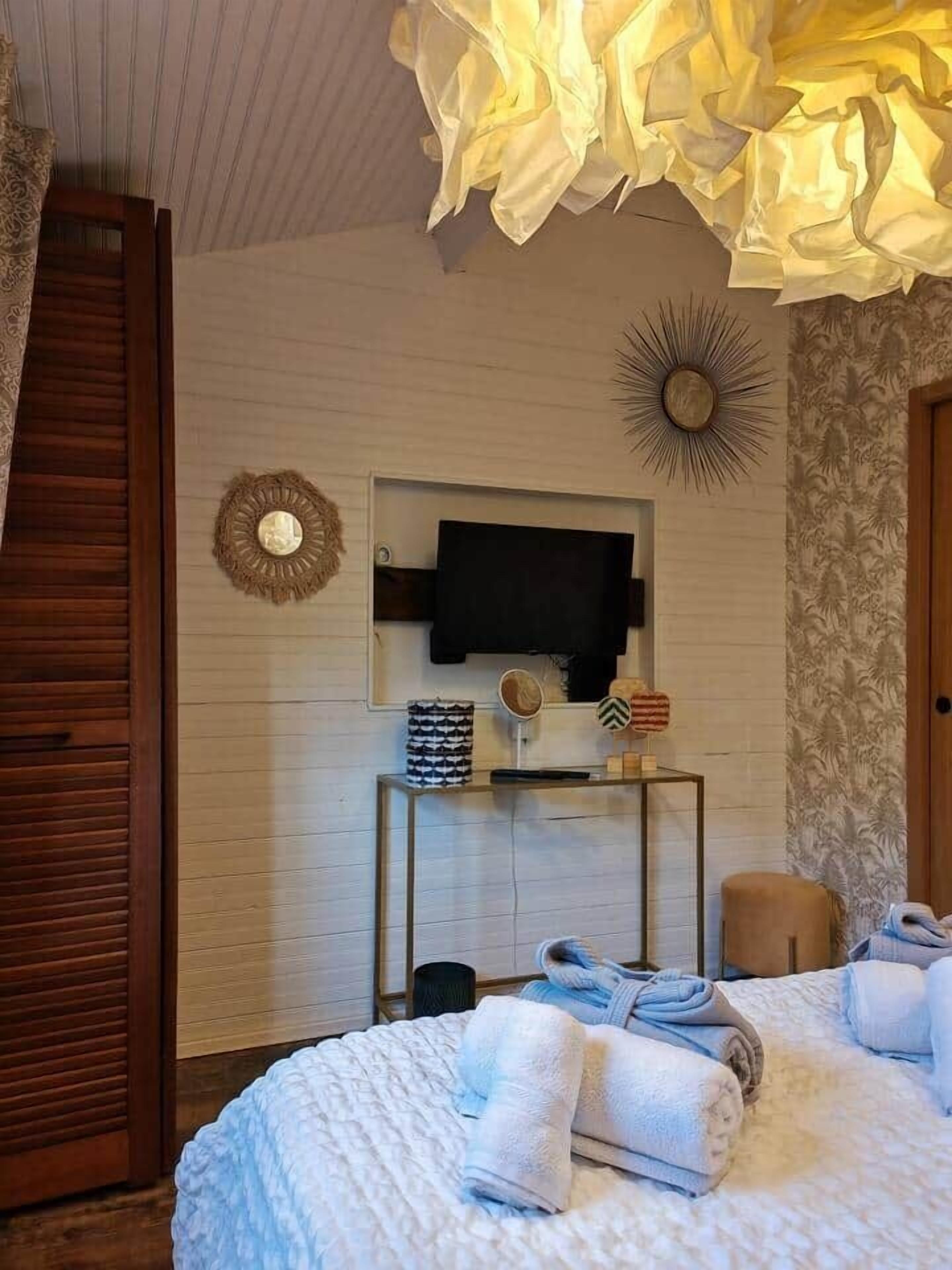 Een slaapkamer met een bed, een aan de muur bevestigde televisie, een nachtkastje met een lamp en een decoratieve spiegel.