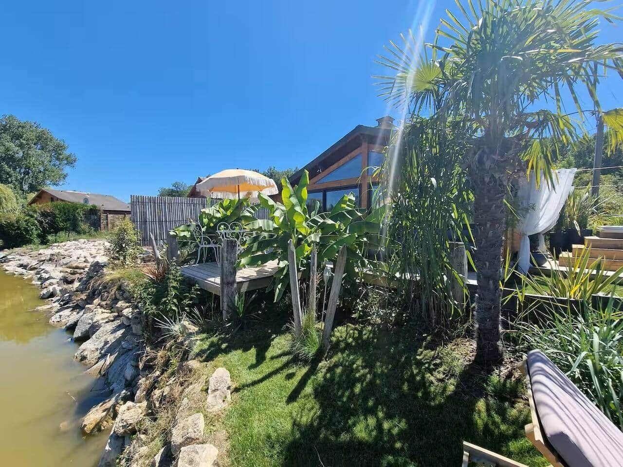 A house with a pond, surrounded by tropical plants and a wooden deck.