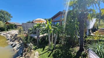 A house with a pond, surrounded by tropical plants and a wooden deck.