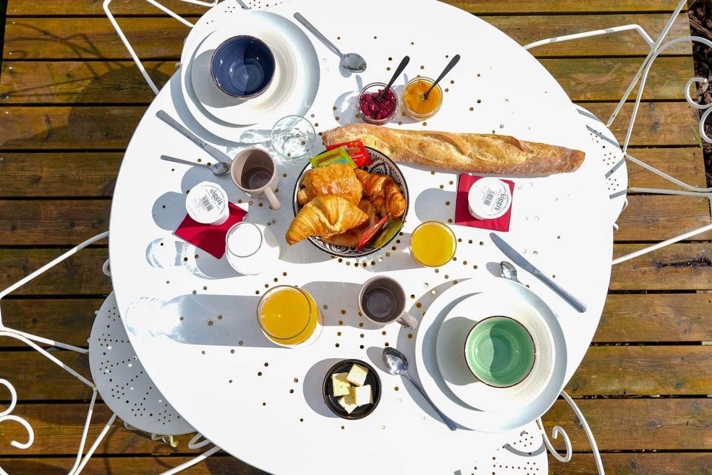 Une table ronde avec un assortiment de produits pour le petit-déjeuner, notamment des croissants, des confitures et des boissons.
