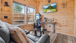 A cozy cabin interior with a leather sofa, a small table with a board game, a window with a view of the outdoors, and wooden walls. - Great place for One or Two, Cozy, Hot Tub, Views (Pigeon Forge)