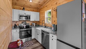 A compact kitchen with wooden walls, white cabinets, stainless steel appliances, and a window providing natural light. - Great place for One or Two, Cozy, Hot Tub, Views (Pigeon Forge)