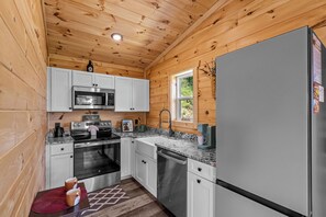 A compact kitchen with wooden walls, white cabinets, stainless steel appliances, and a window providing natural light. - Great place for One or Two, Cozy, Hot Tub, Views (Pigeon Forge)