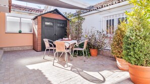Eine Terrasse mit Tisch und Stühlen, ein kleines Gartenhaus und Kübelpflanzen.