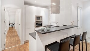 Een moderne keuken met witte kasten, een ingebouwde oven en een groot kookeiland met barstoelen.