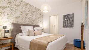 Een slaapkamer met een bed, nachtkastje, lamp, hanglamp, kledingkast, poef in blauw en een houten vloer.