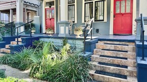 A two-story building with a red door, a number 4418, and a small garden area with steps leading up to the entrance. - Spacious 3BR Home w/ Heated Pool in the Heart of New Orleans (New Orleans)