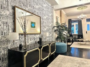 A modern living room with a black and gold console, a large mirror, and a patterned wall. - Magnolia Manor Mid-City Home w/ Heated Pool (New Orleans)