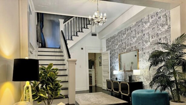 A spacious living room with a staircase, a large mirror, and a black console table. - Spacious 3BR Home w/ Heated Pool in the Heart of New Orleans (New Orleans)