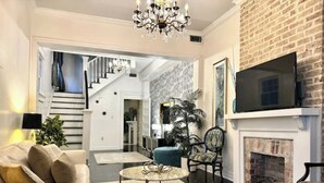 A spacious living area with a fireplace, a staircase, and a television mounted on the wall. - Spacious 3BR Home w/ Heated Pool in the Heart of New Orleans (New Orleans)
