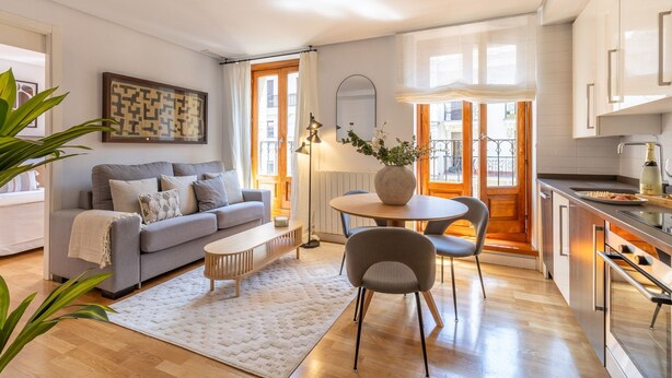 A modern living room with a sofa, coffee table, and dining area. There is a kitchen with a sink and a bottle of champagne. - Cozy Apartment for Two in Alcalá Area (Madrid)