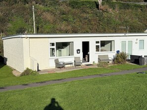 Ein Bungalow mit Terrasse, einem kleinen Garten und Blick auf einen Hügel.