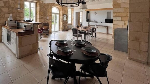 A spacious kitchen with a dining area, stone walls, and a modern pendant light. - Entre vignes et océan (Jau-Dignac-et-Loirac)