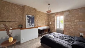 A bedroom with a stone wall, a bed, a desk, and a window. - Entre vignes et océan (Jau-Dignac-et-Loirac)