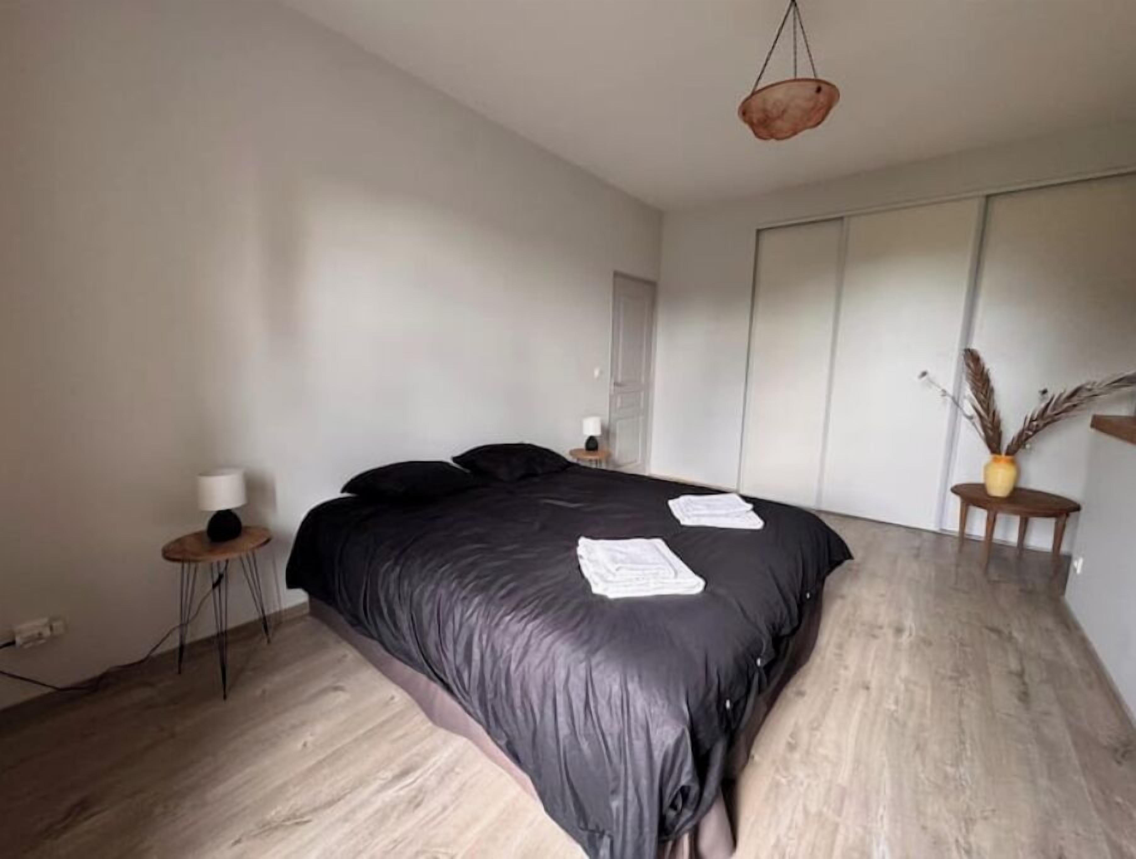 Une chambre moderne avec un grand lit, une table de chevet avec une lampe et un vase contenant des plantes séchées.