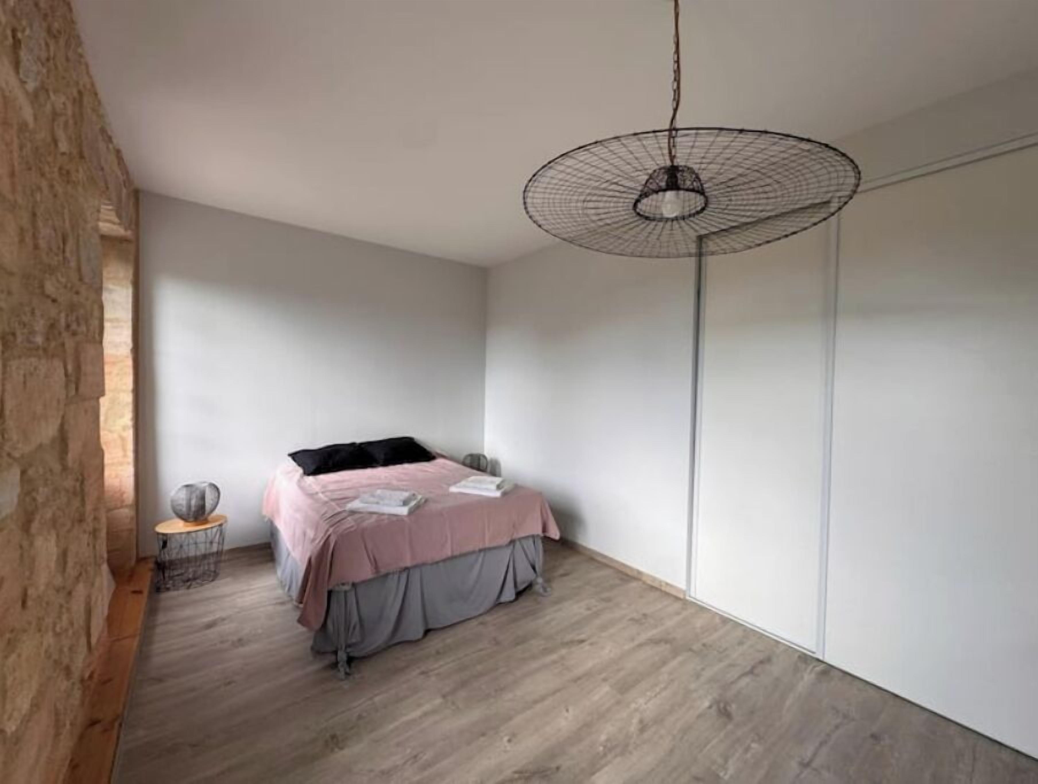Une chambre à coucher au style minimaliste, avec un lit, un luminaire suspendu et un mur en pierre.