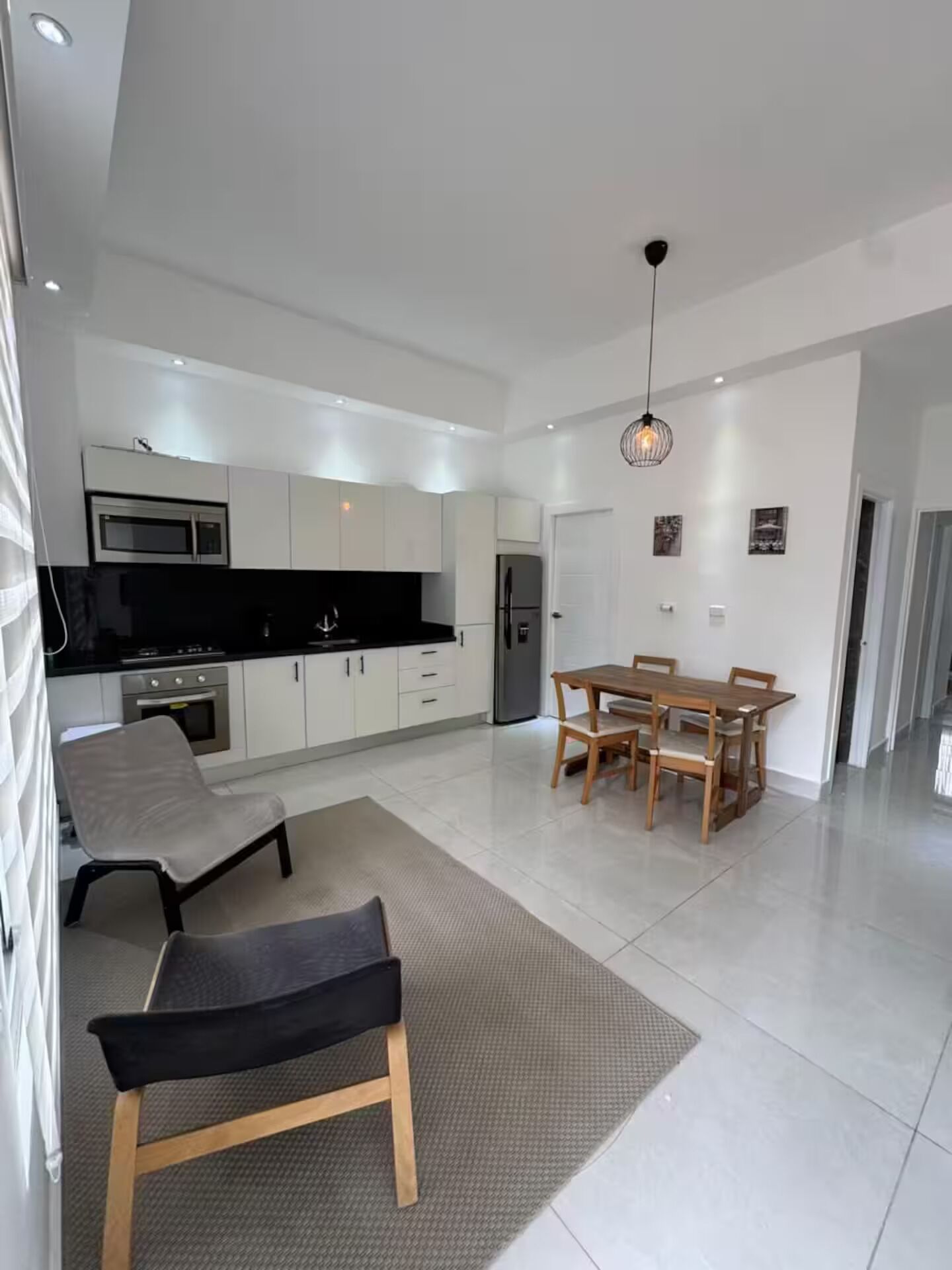A modern kitchen with white cabinets, a black countertop, and stainless steel appliances. There is a dining area with a wooden table and chairs.