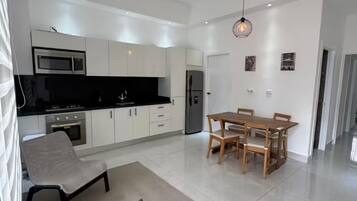 A modern kitchen with white cabinets, a black countertop, and stainless steel appliances. There is a dining area with a wooden table and chairs.