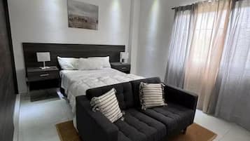 A modern bedroom with a large bed, a dark sofa, and a ceiling fan.