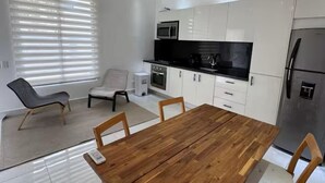 Moderni keittiö, jossa on valkoiset kaapit, puinen ruokapöytä ja riippuvalaisin.