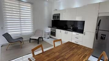 A modern kitchen with white cabinets, a wooden dining table, and a hanging light fixture.