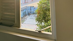 Une fenêtre avec des stores blancs, une vue sur une rue bordée d’immeubles et un chantier de construction.