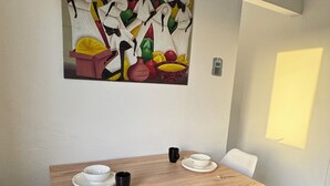 Un coin repas avec une table en bois, des chaises blanches et un tableau abstrait aux couleurs vives accroché au mur.