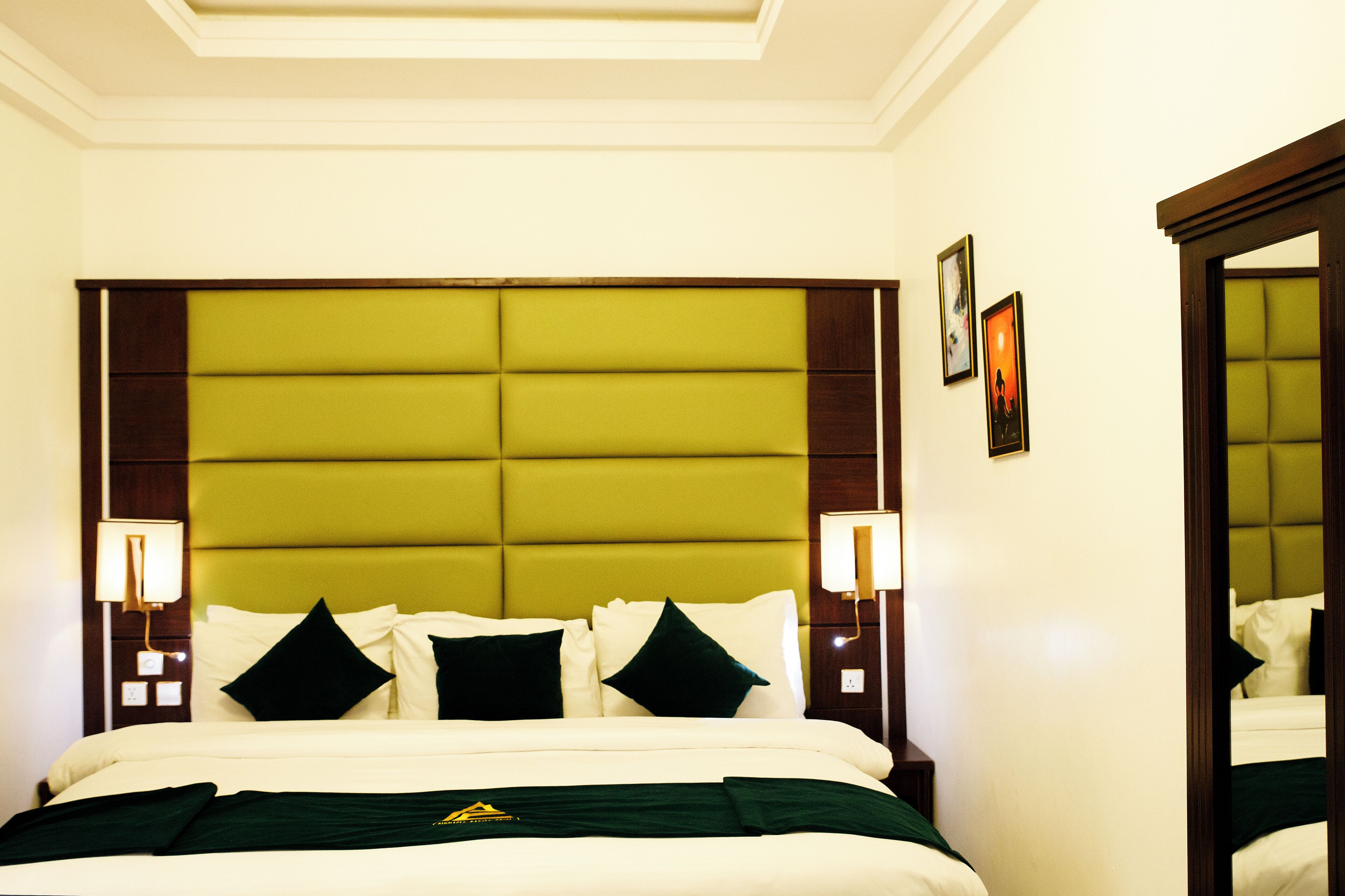 A hotel room with a large bed, green headboard, white bedding, and two bedside lamps.